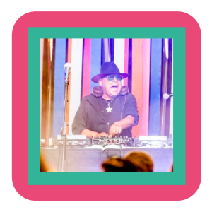 DJ wearing hat at mixing console, colorful backdrop.
